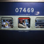 A passenger looks out of a carriage window as the passenger opposite him lies on his seat on the Abohar-Jodhpur passenger train also known by the locals as the Cancer Express in Bhatinda, Punjab. [Prashanth Vishwanathan (Bloomberg)]